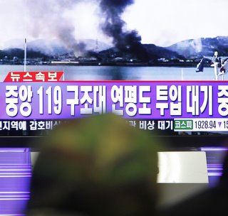 South Koreans watch news on television showing smoke rising from Yeonpyeong Island after it was hit by dozens of artillery shells fired by North Korea, at Seoul railway station