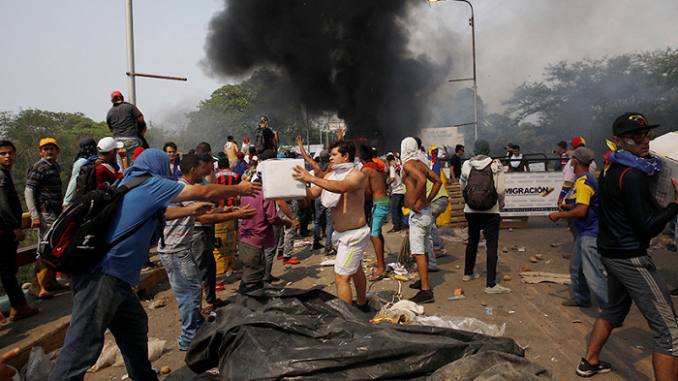 Voluntarios tratan de sal salvar parte de la ayuda humanitaria en el incendio de un camión.